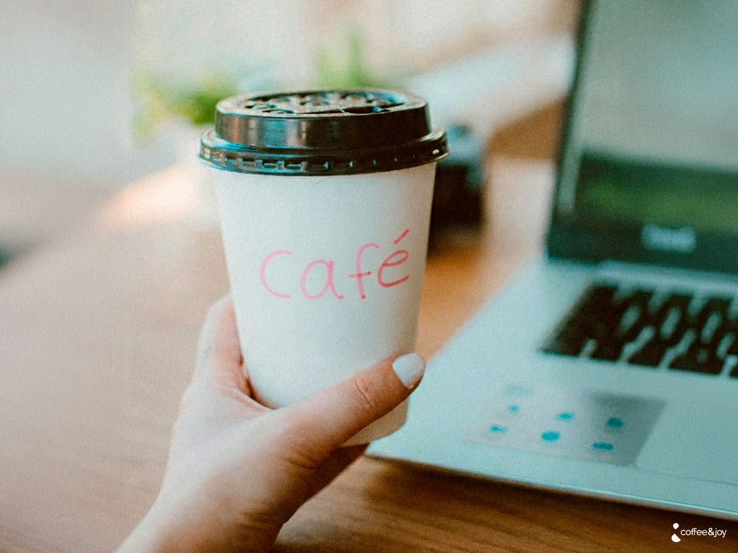 Café para viagem em copo descartável ao lado de notebook, representando consumo de café no trabalho.