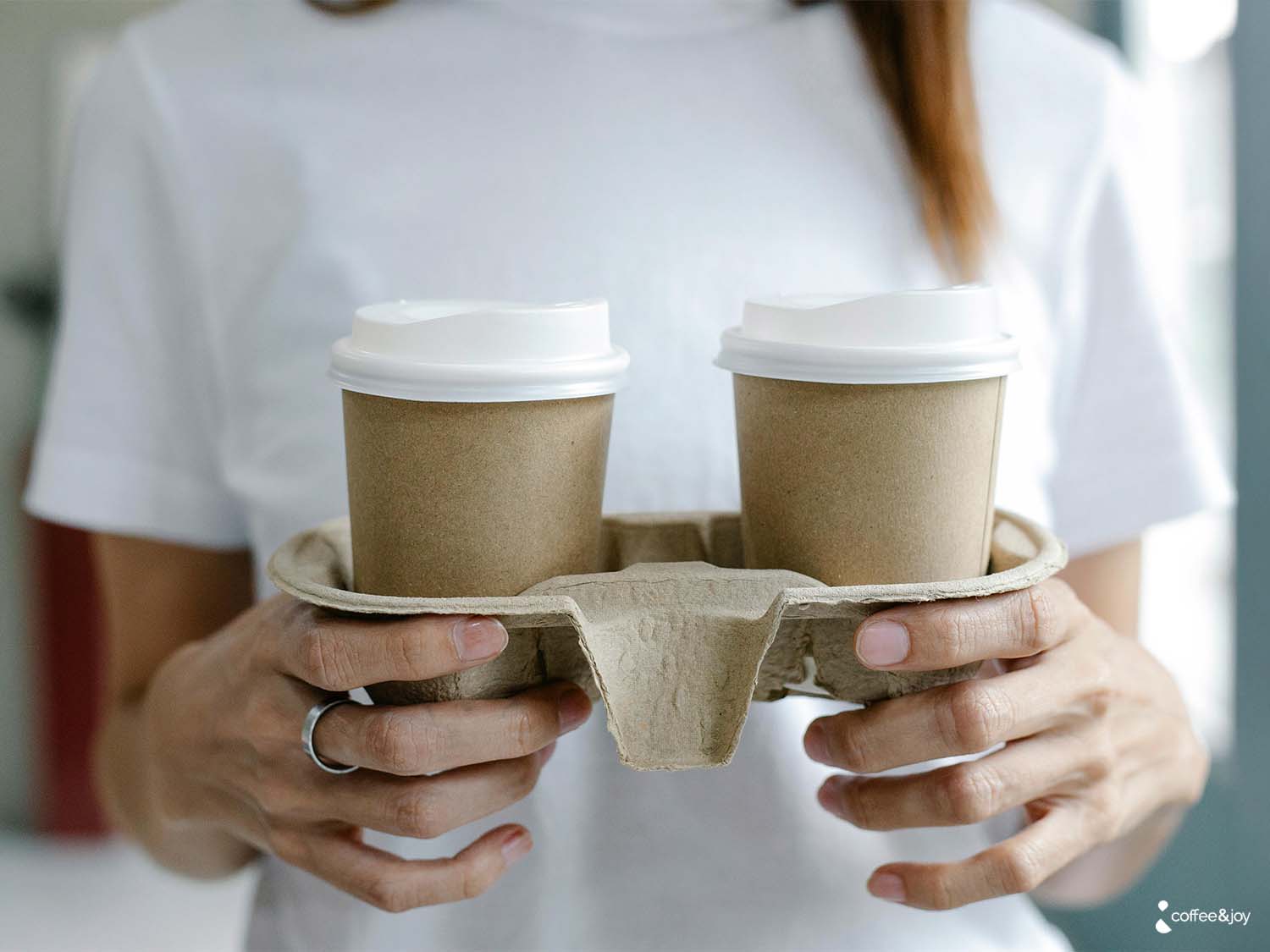 Cafés para viagem em copos descartáveis sendo transportados por uma pessoa.